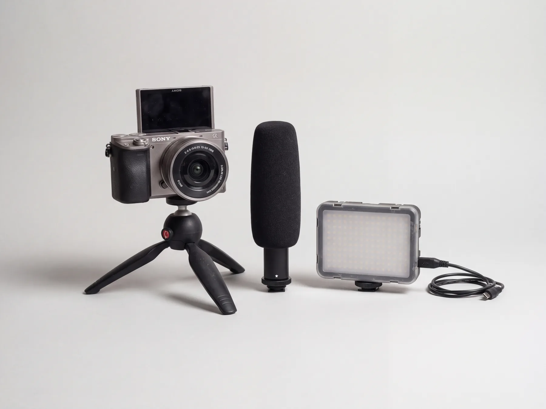 Vlogcamera, shotgun-microfoon en LED-lamp naast elkaar op een lichtgrijze ondergrond